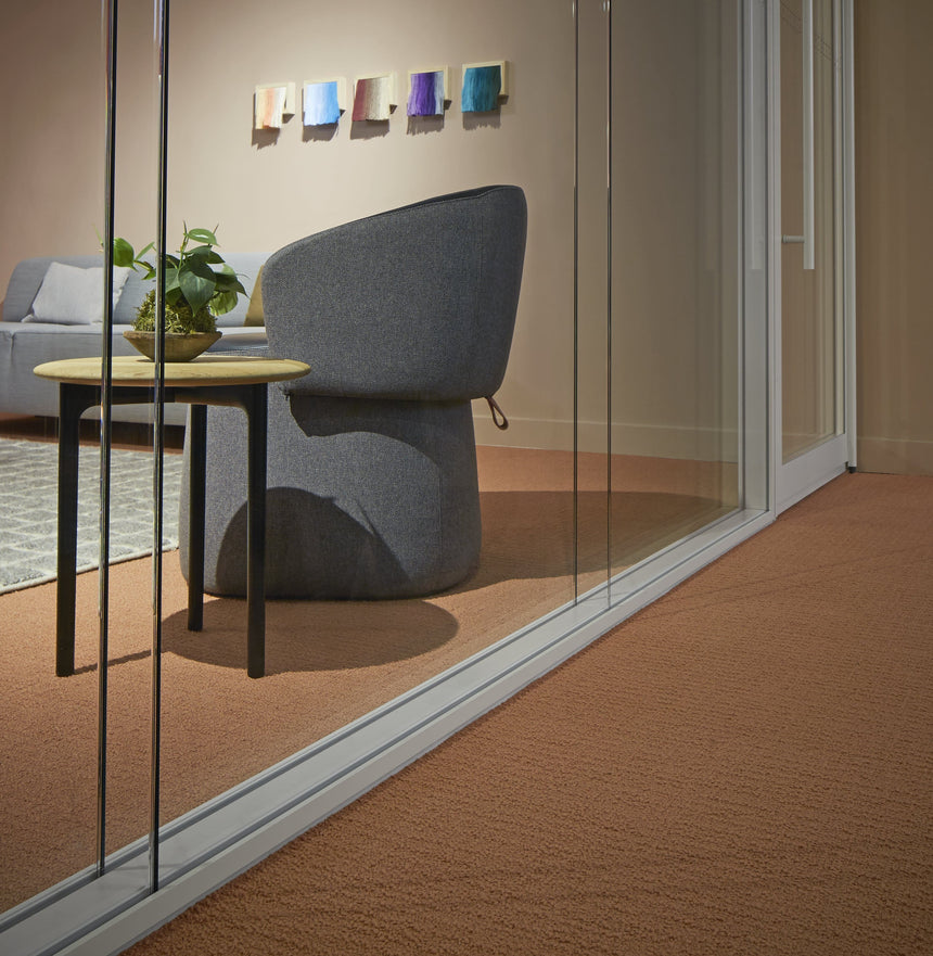 Modern office chair in a glass-walled room with a small table and plant.