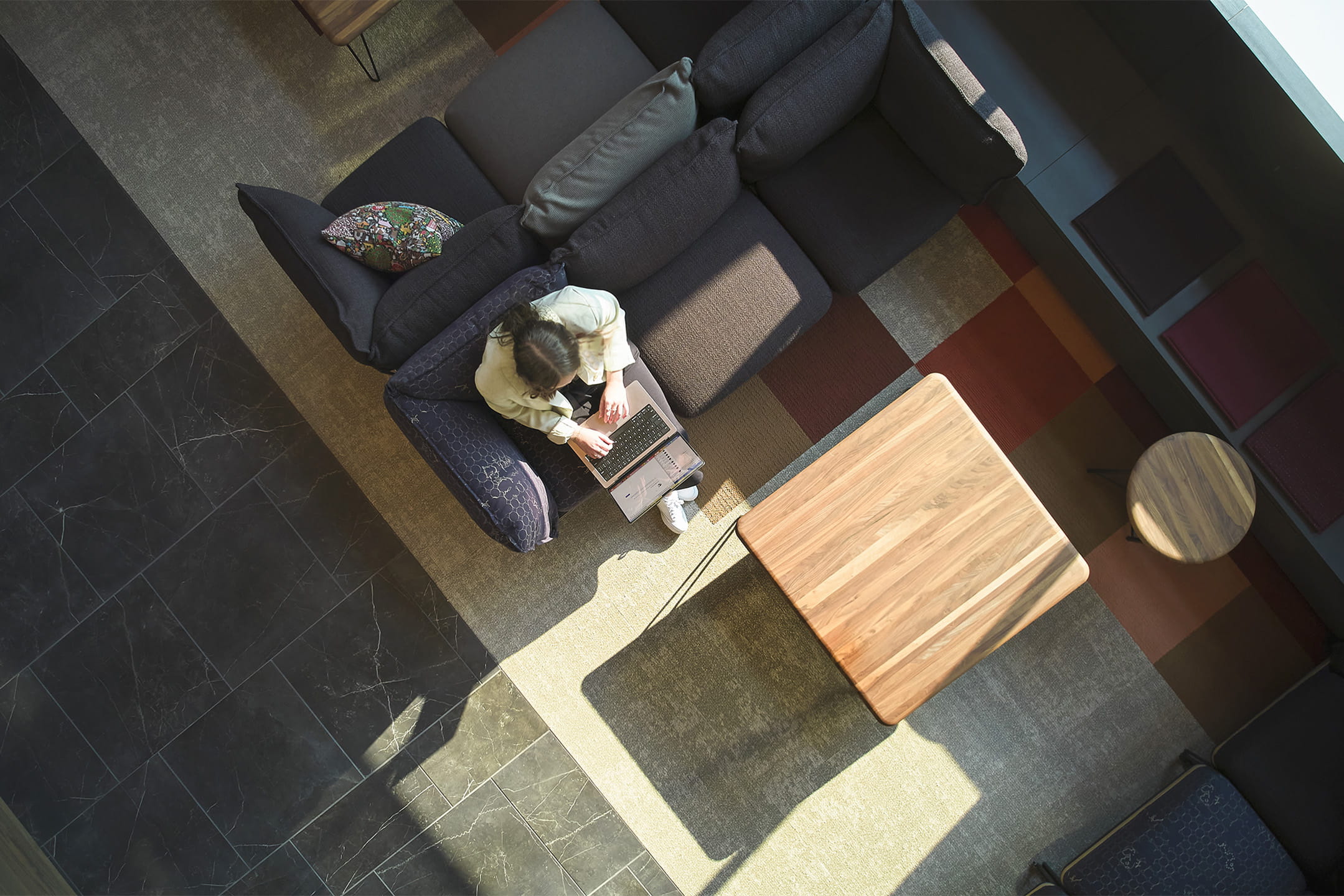 Person sitting on a gray sectional sofa in a modern living room with a wooden coffee table.
