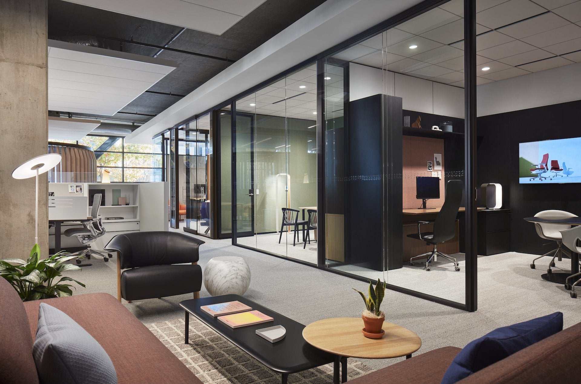Modern office interior with glass walls, furniture, and a TV screen.