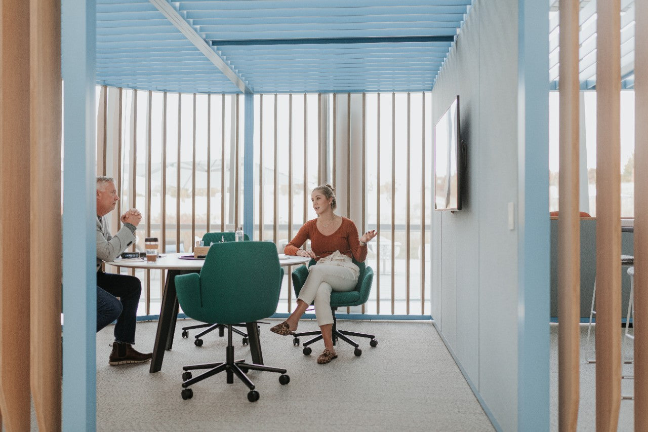 Two people sitting at a table in a modern office setting with blue walls and chairs.