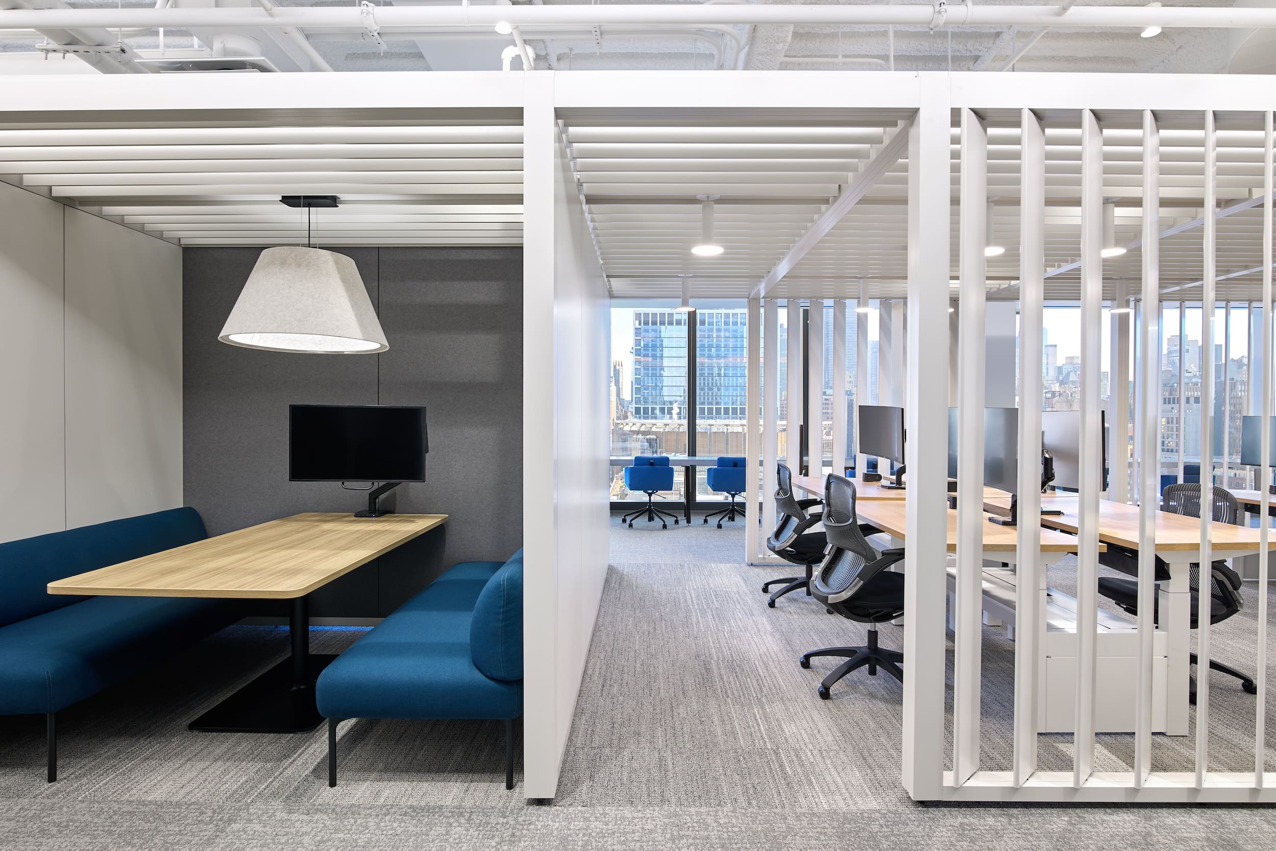 Modern office space with blue couches, wooden tables, and glass partitions.
