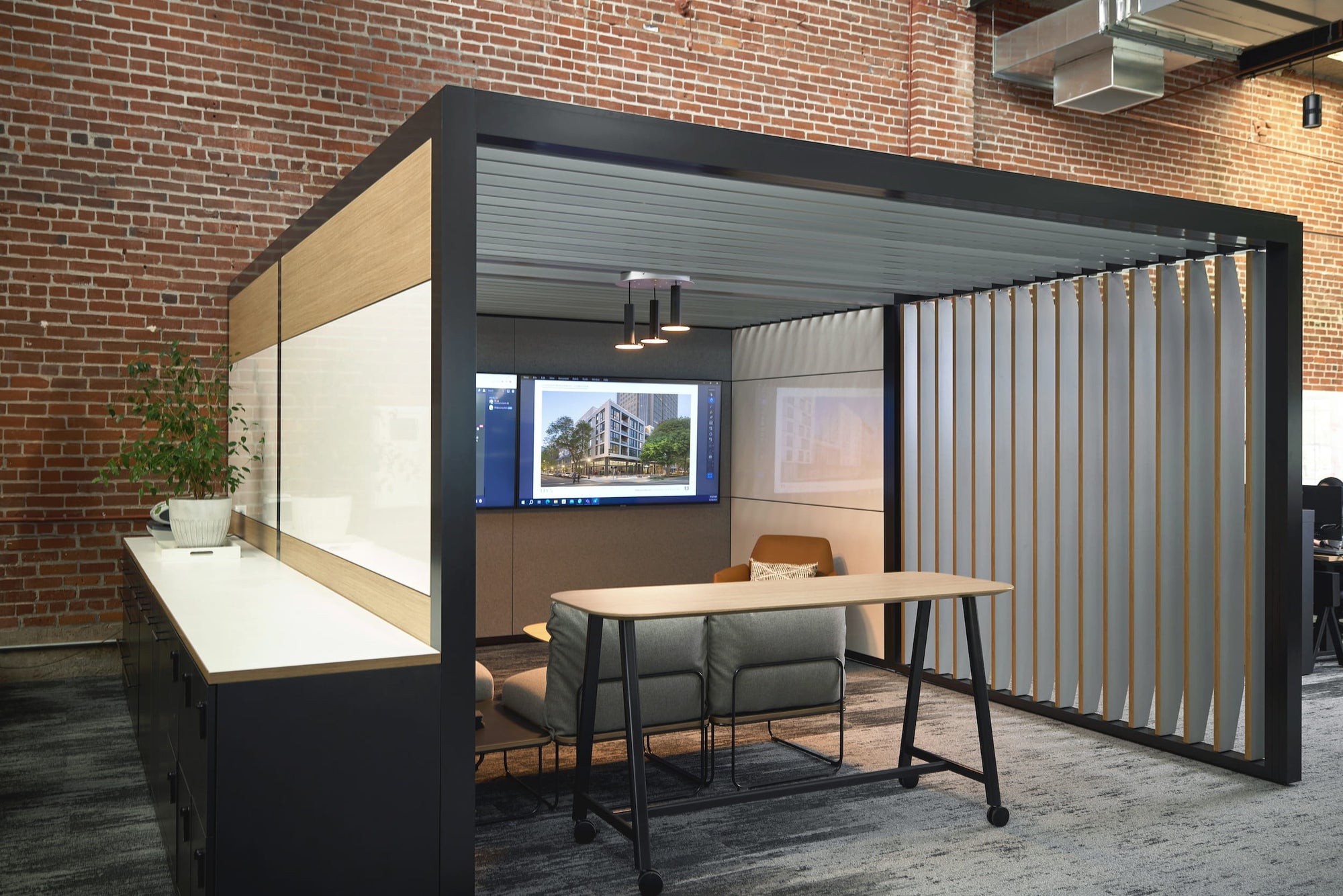 Modern office partition with a desk and chairs in front of a brick wall.