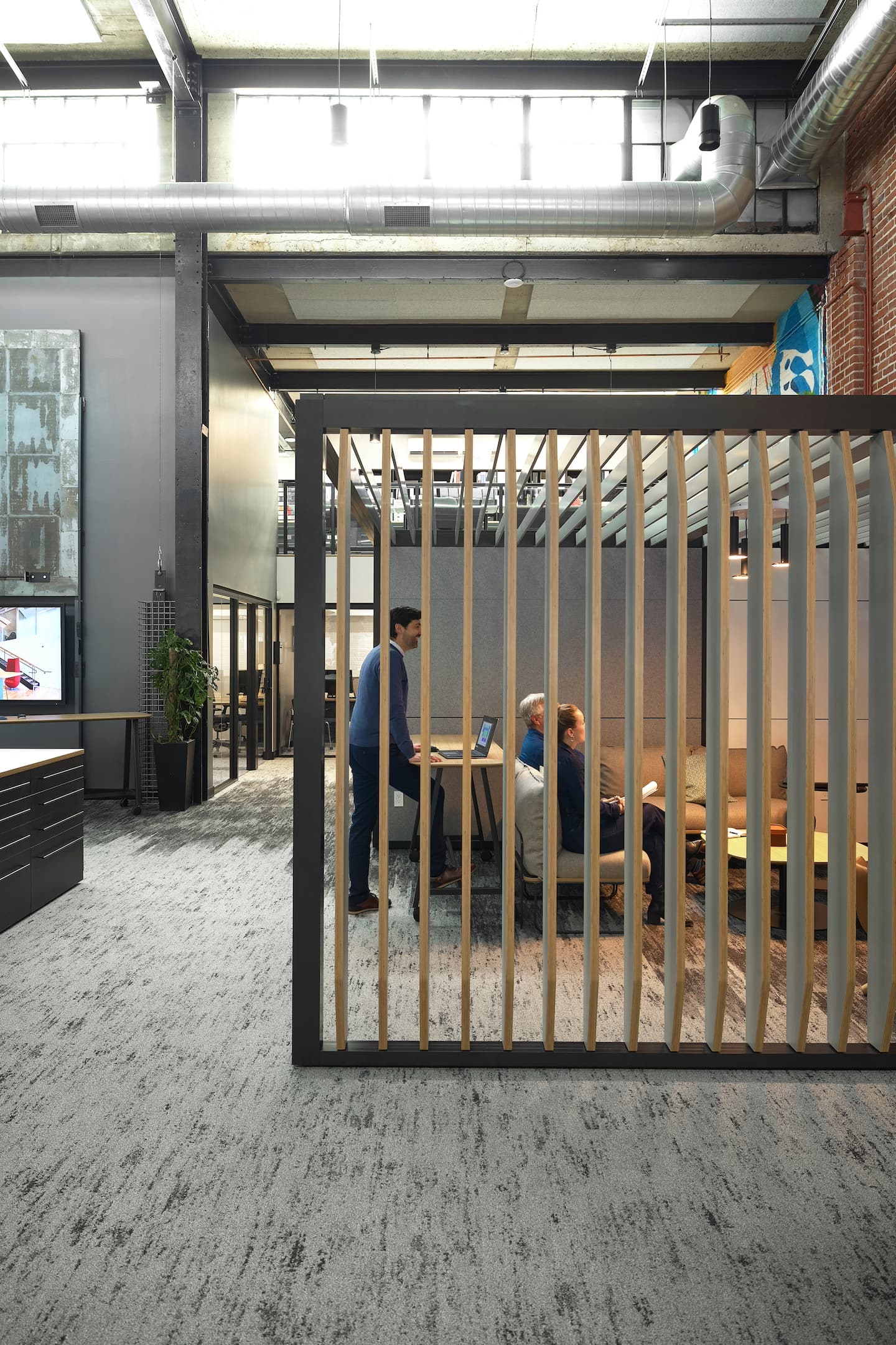 Modern office interior with people working at a desk, viewed through a glass partition.