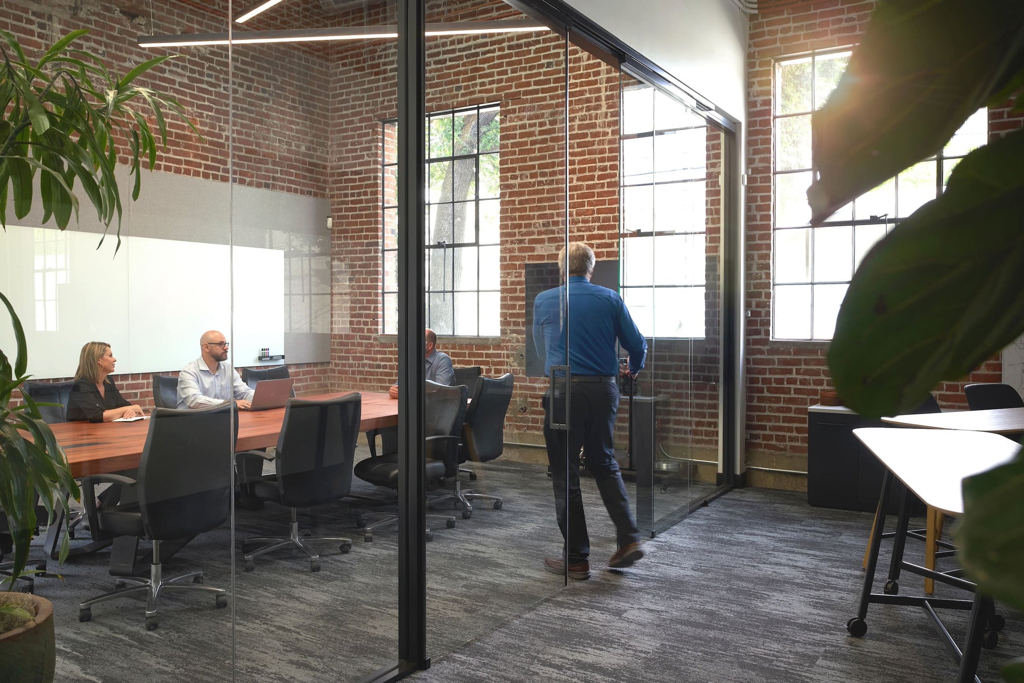 Modern office with glass walls and brick walls, people working at desks.