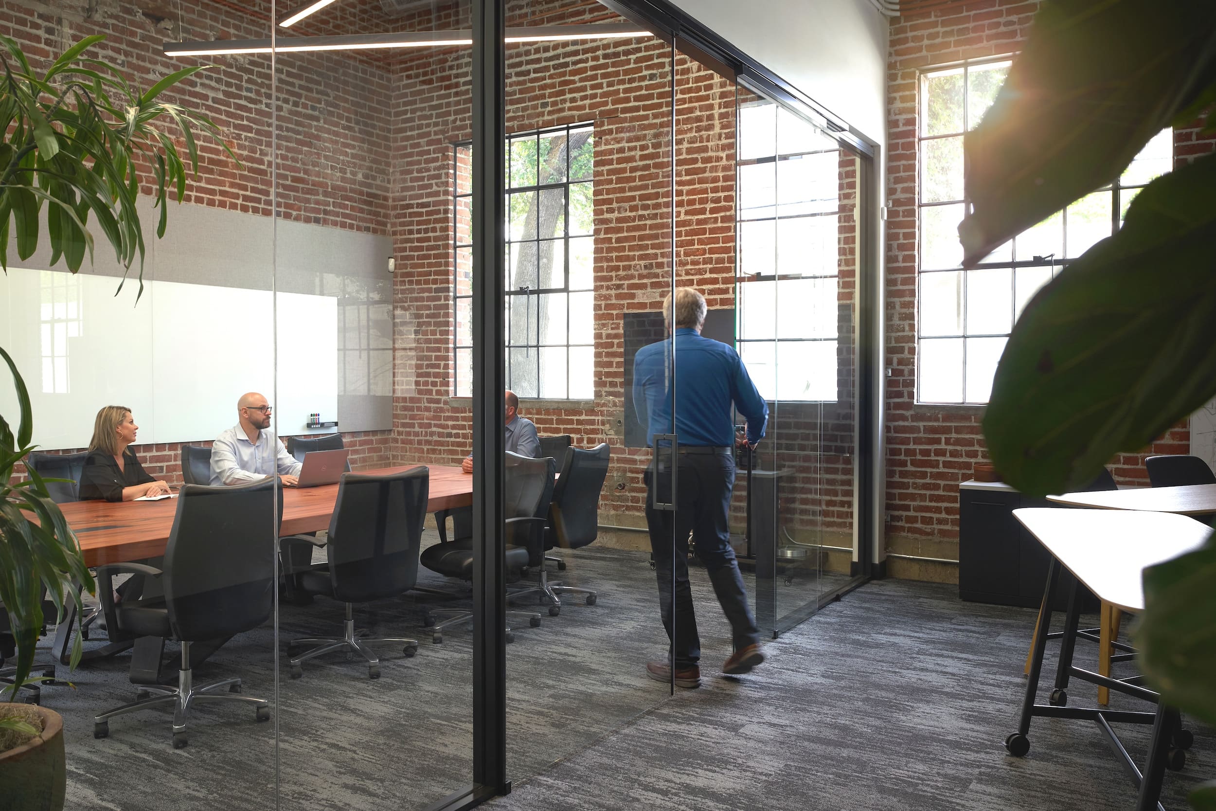 Modern office with glass walls and brick walls, people working at desks.