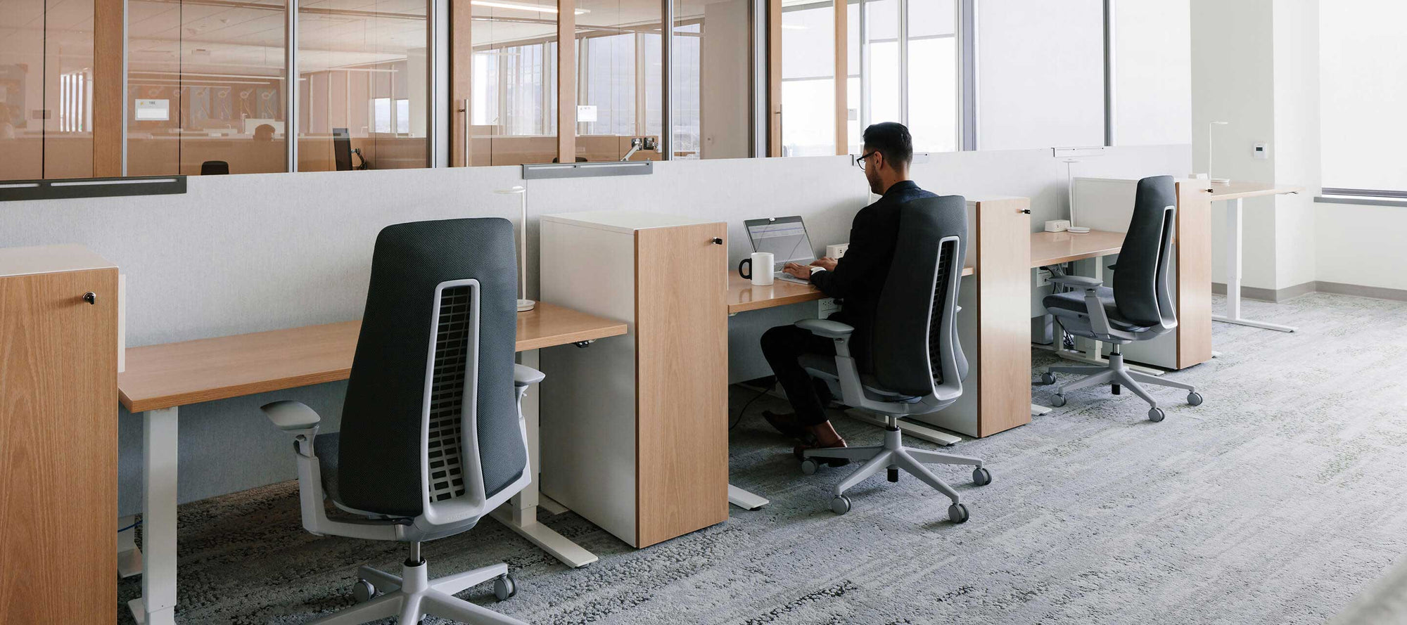 Person working at a desk in a modern office with glass walls and chairs.