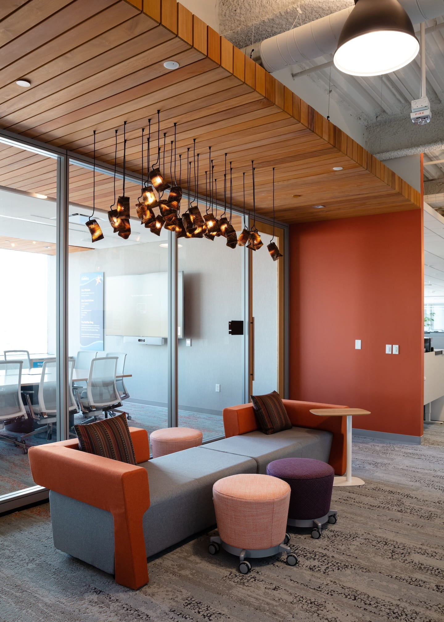 Modern office interior with a gray and orange sofa, ottomans, and a chandelier.