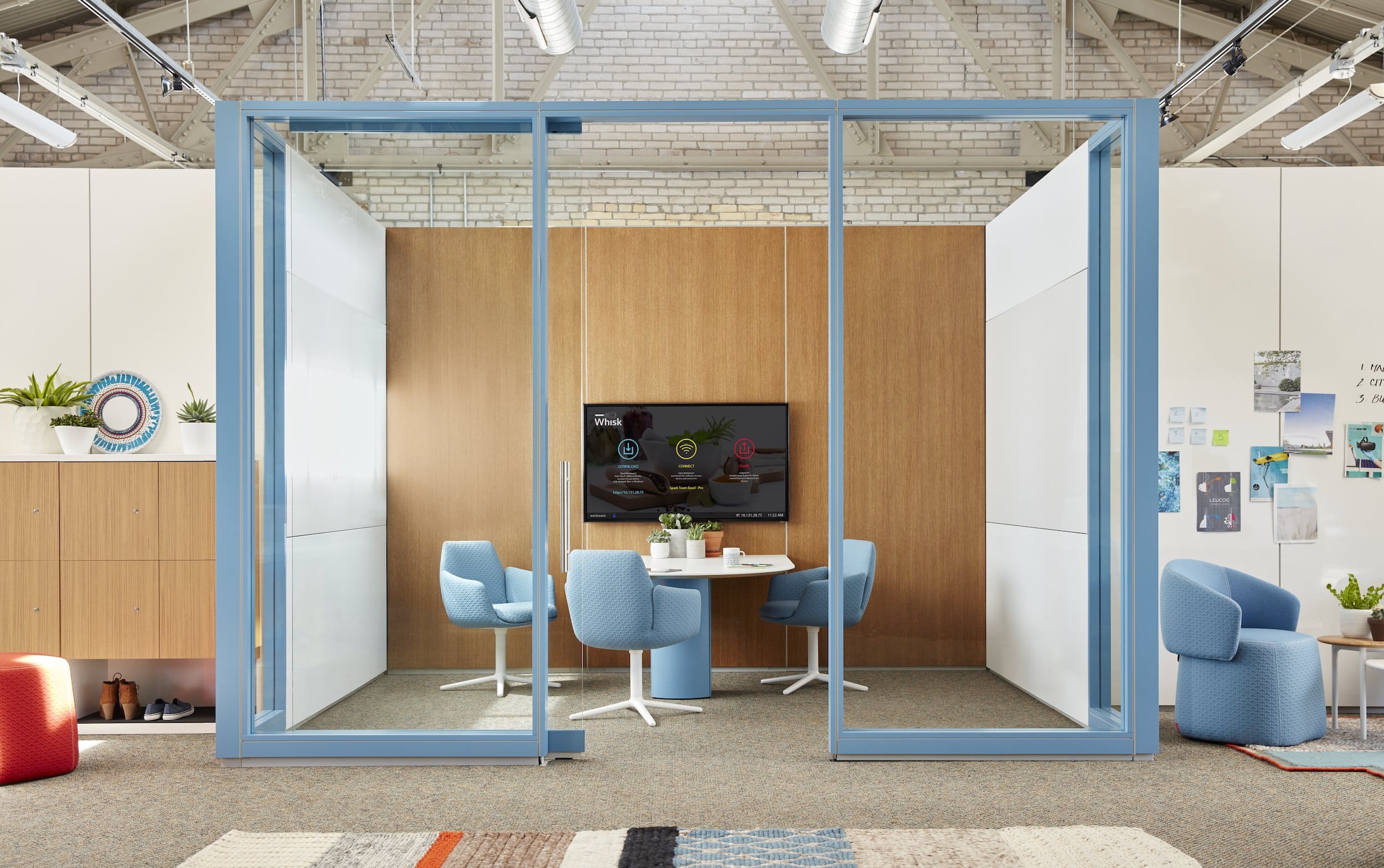 Modern office space with glass partition, chairs, and a TV screen.
