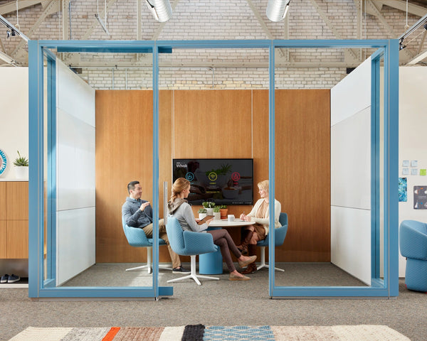 Modern office space with glass partition and people sitting at a table.