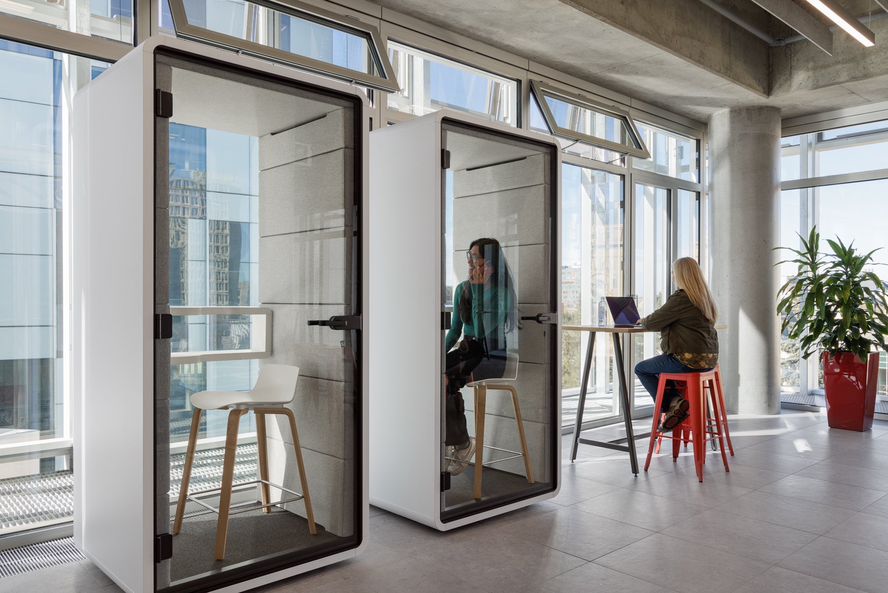 Two white office pods with glass walls in a modern office setting.
