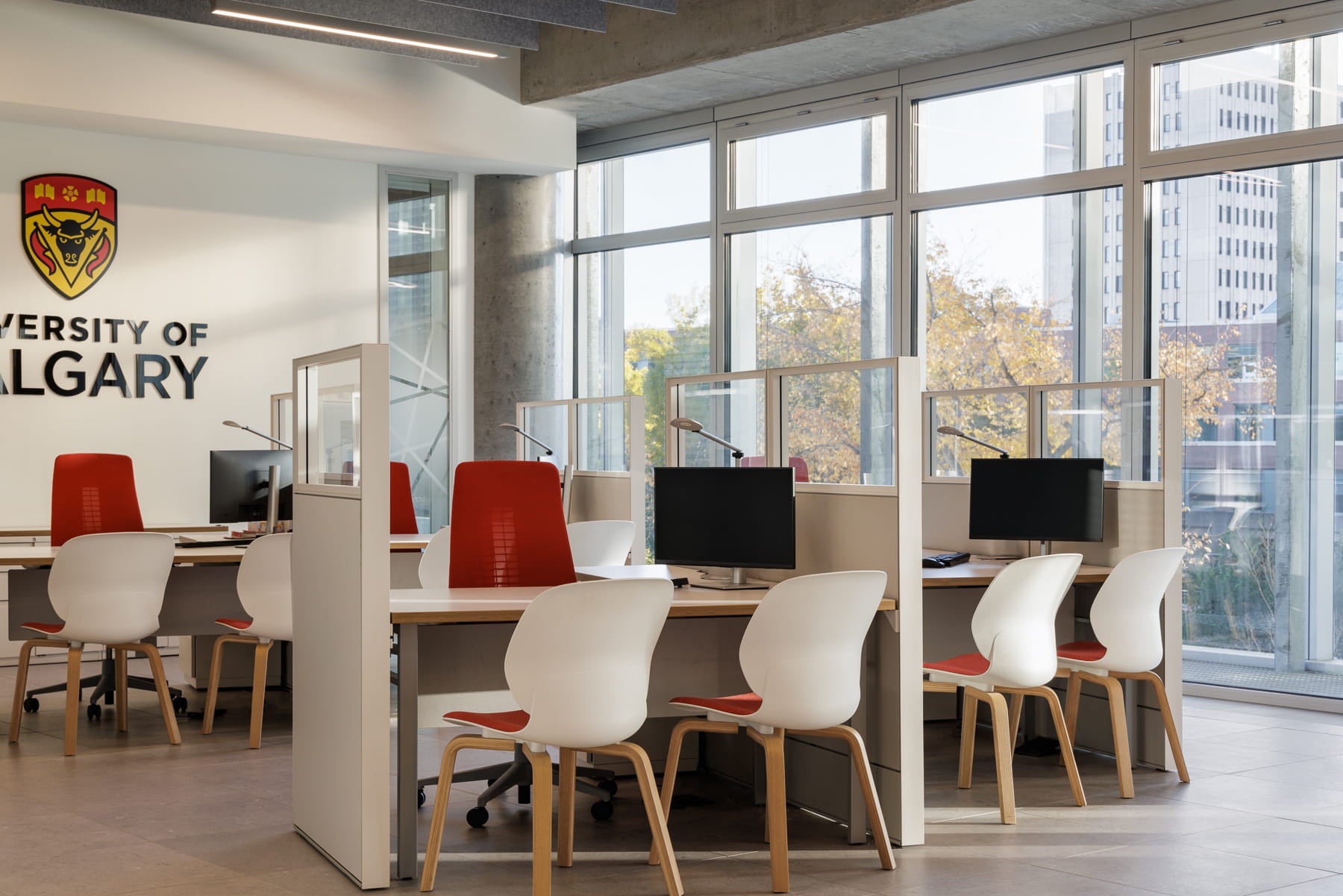 Modern office space with desks, chairs, and computer monitors in a room with large windows.