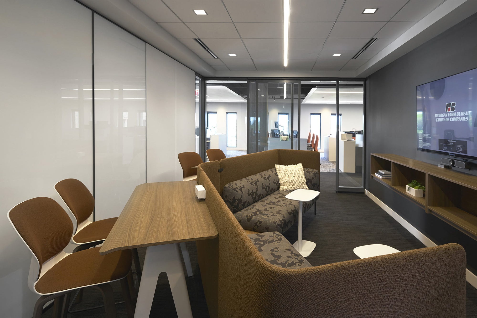 Modern office waiting area with brown chairs, a wooden table, and a TV on a shelf.